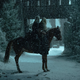 Two people with long, silvery-blonde hair sit atop the same horse in a snowy landscape.